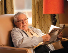 Elderly man reading a newspaper while sitting on a chair